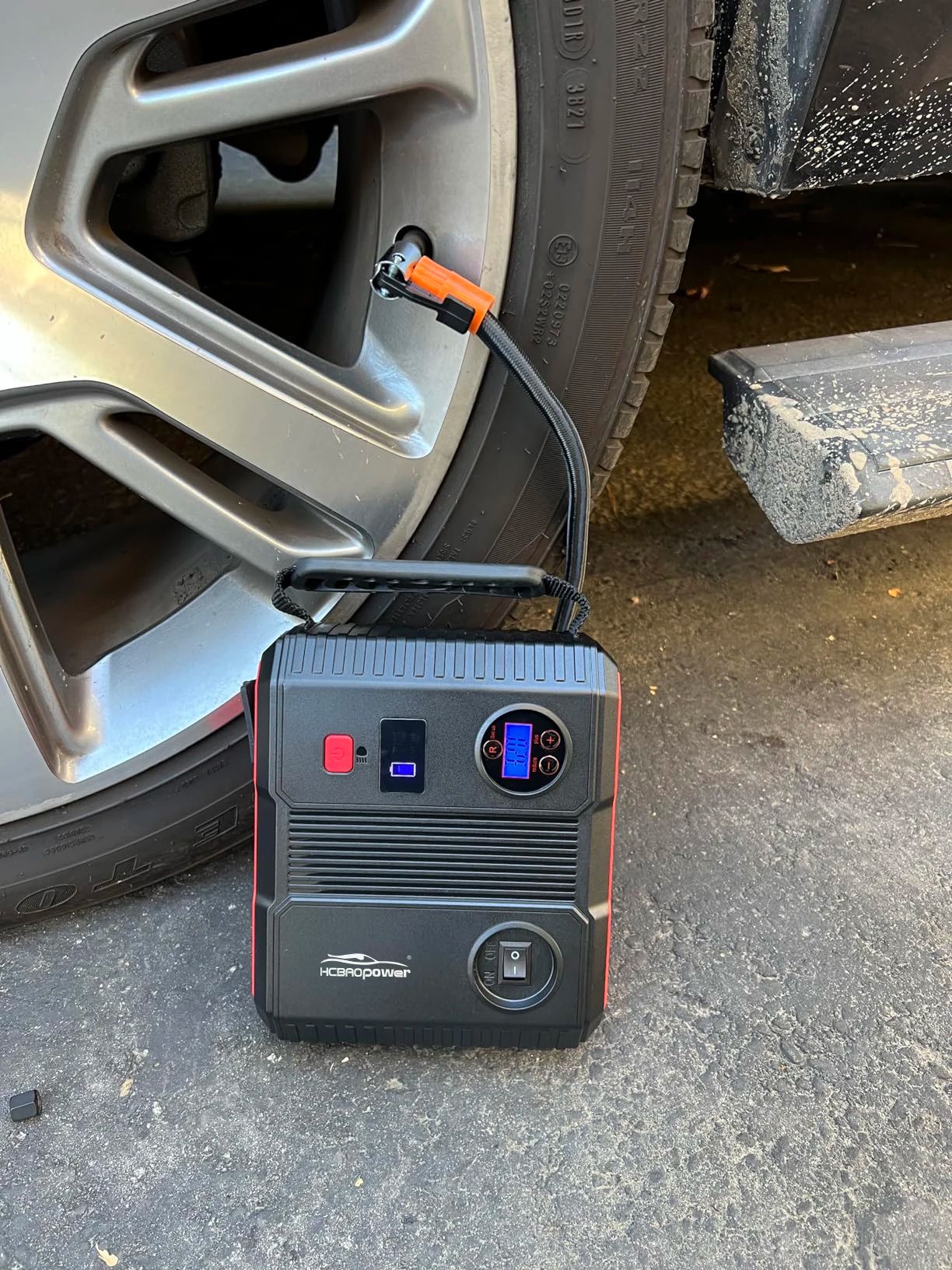 Portable jump starter charging a smartphone and using LED SOS light during a night breakdown.